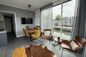Una sala de estar moderna con comedor, televisor de pantalla plana en la pared y un ventanal con vistas al exterior.