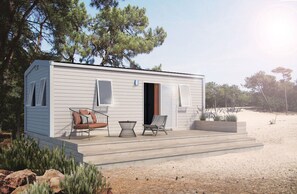 A single-story mobile home with a porch, two chairs, a small table, and a door leading to the interior.