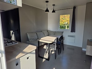 Cocina compacta con comedor, estufa integrada y ventana con cortinas.