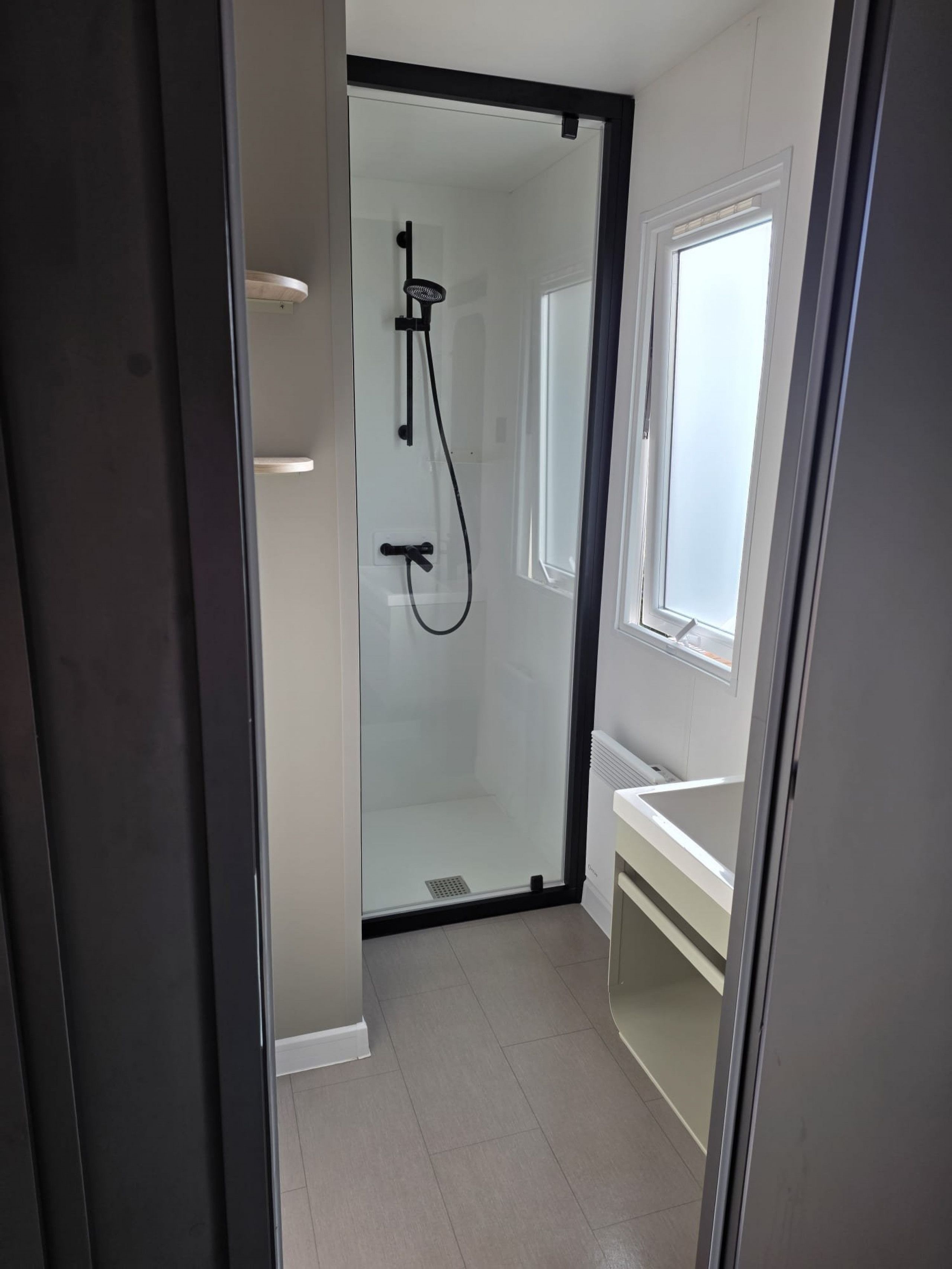 Une salle de bain moderne avec une douche à parois de verre, un lavabo blanc et une fenêtre.