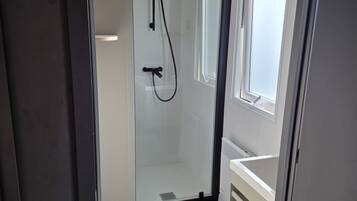 Une salle de bain moderne avec une douche à parois de verre, un lavabo blanc et une fenêtre.