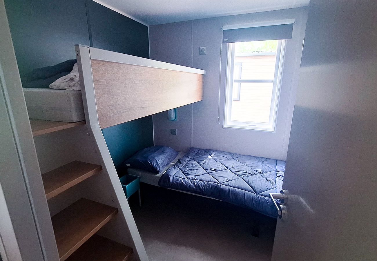Une petite pièce avec un lit superposé, une fenêtre et une étagère intégrée.