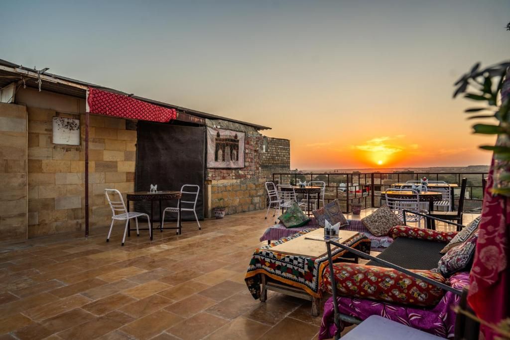 An outdoor seating area with tables and chairs, a view of the sunset, and a building with a brick facade.