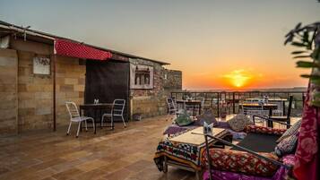An outdoor seating area with tables and chairs, a view of the sunset, and a building with a brick facade.