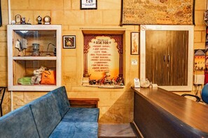Ein Empfangsbereich mit einer Holztresen, einem blauen Sofa, einer Glastausche und einem an der Wand befestigten Schild, das Dienstleistungen wie Wüstensafari und Stadtführung auflistet.