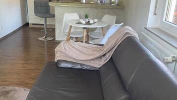 Een moderne woonkamer met een donker leren bank, een klein rond tafeltje met stoelen, en een keuken op de achtergrond.