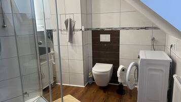 Een moderne badkamer met een douchecabine van glas, toilet en wasmachine.