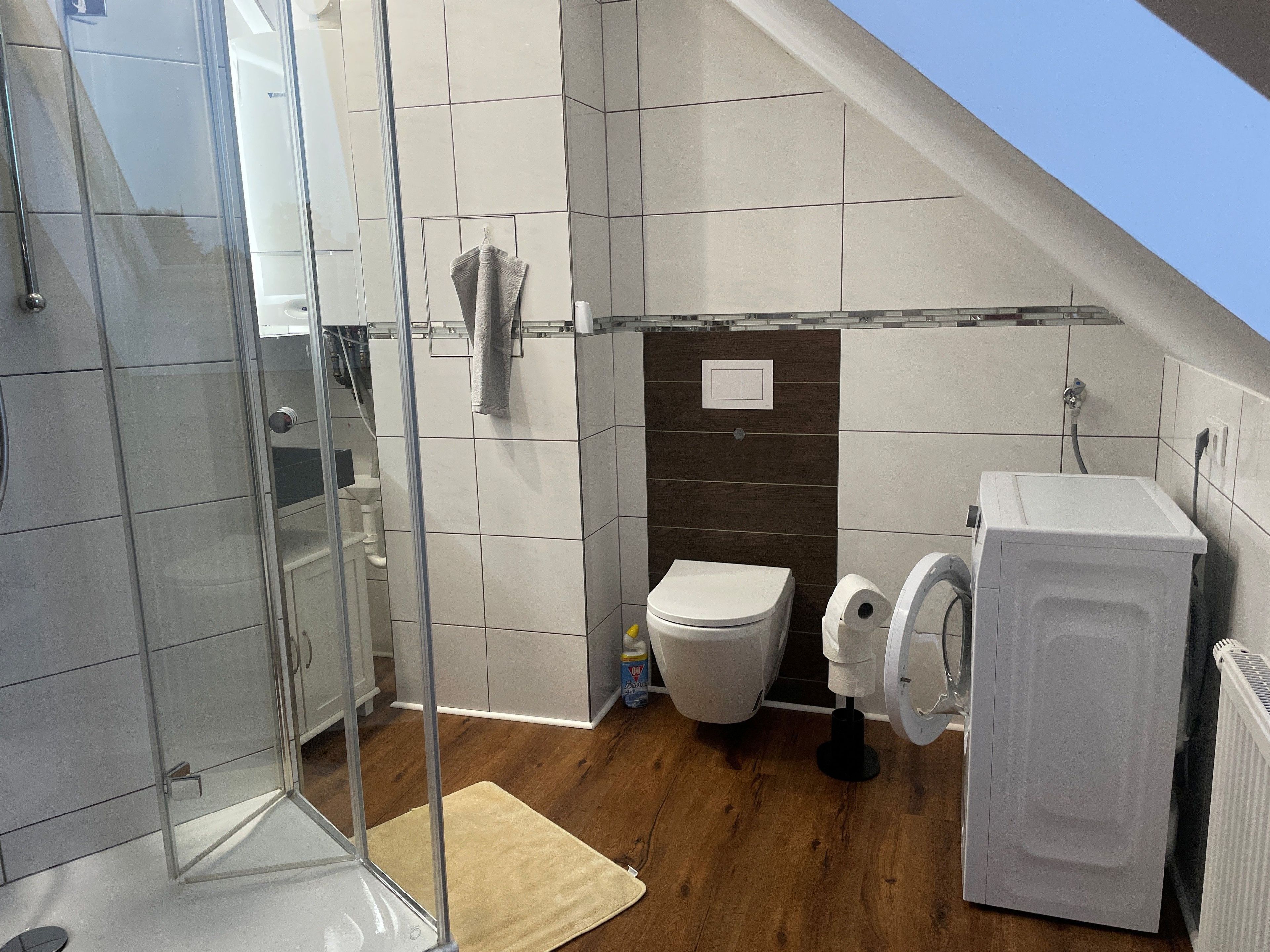 Ein modernes Badezimmer mit Duschkabine aus Glas, Toilette und Waschmaschine.