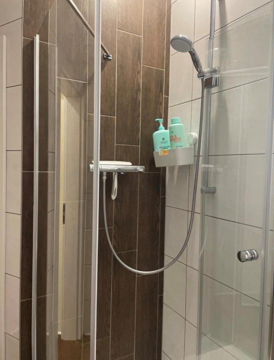 Ein Duschbereich mit Glasabtrennung, einer Handbrause und einem am Wand montierten Wasserhahn.