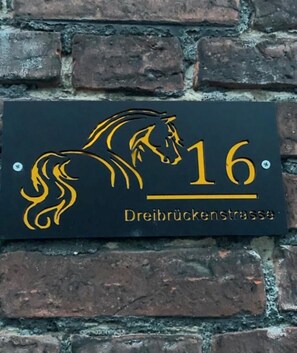 A black sign with a gold horse silhouette and the number 16, indicating a location or property named Dreibrückenstrasse. - Vacation Rentals at the "Landgestüt," Apartment at the Landgestüt, 55 m², 1–3 people (Warendorf)
