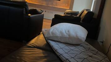 Ein modernes Wohnzimmer mit einer Couch, einem Relaxsessel, einem an der Wand befestigten Fernseher und einer gemusterten Decke auf dem Boden.