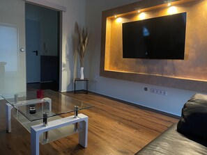 A modern living room with a flat-screen TV mounted on a wall, a glass coffee table, and a wooden floor. - Vacation Rentals at the "Landgestüt," Apartment at the Landgestüt, 55 m², 1–3 people (Warendorf)