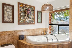 Un bagno con una vasca da bagno ampia, un quadro appeso al muro e vista su del verde all'esterno.