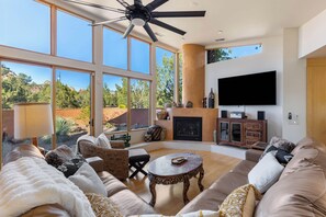 A spacious living room with a large sofa, a fireplace, a flat-screen TV, and a ceiling fan. - West Sedona 4BR retreat with hot tub, game room, and red rock views. (Sedona)