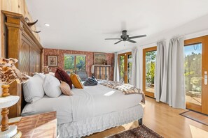 Ein Schlafzimmer mit einem großen Bett, einem Deckenventilator, einem Fenster mit Vorhängen und Blick ins Freie.