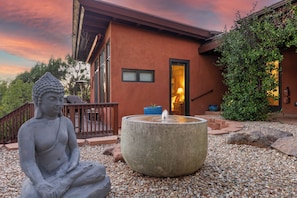 A Buddha statue in a garden with a stone fountain, a wooden deck, and a building with a door and windows. - West Sedona 4BR retreat with hot tub, game room, and red rock views. (Sedona)