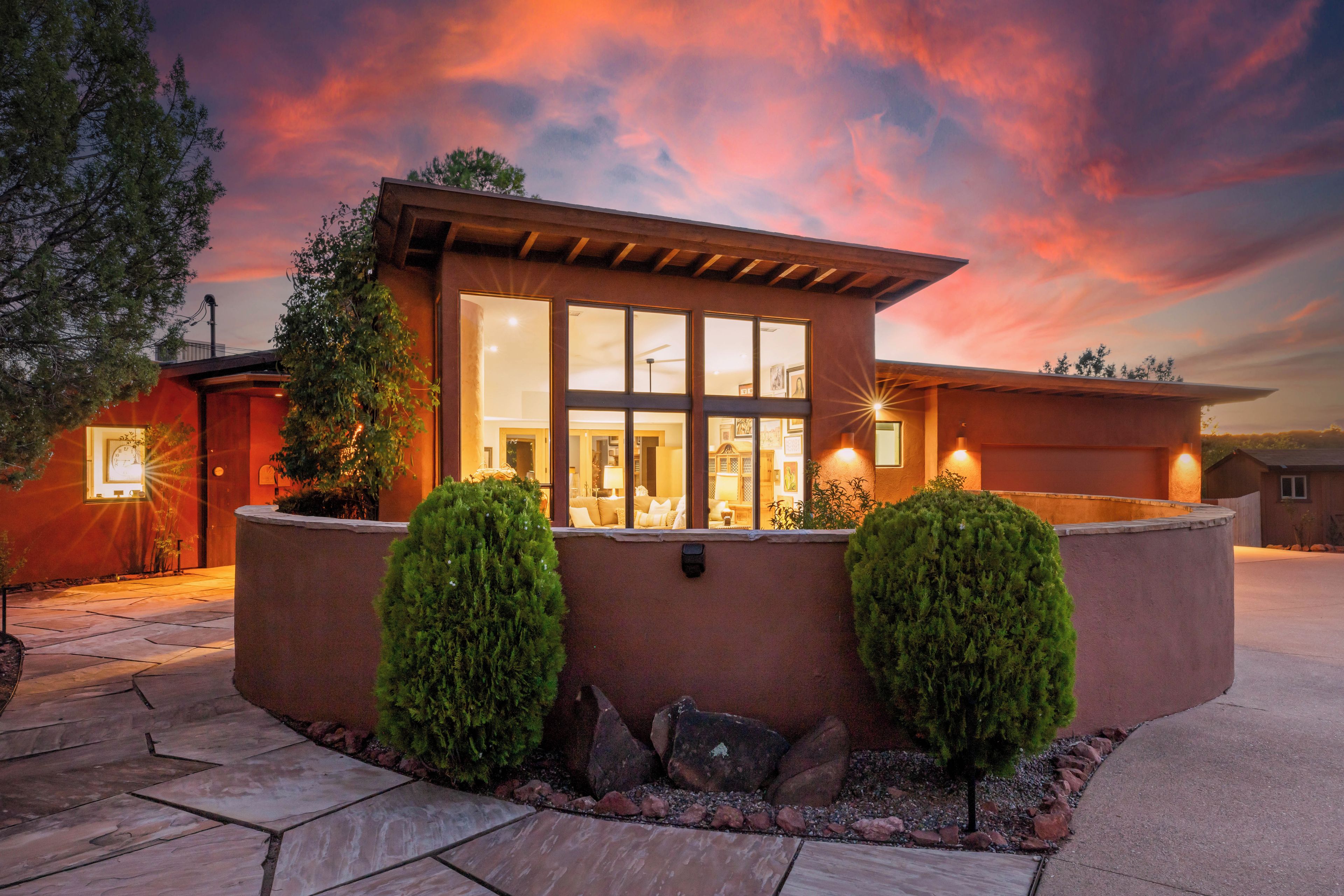 A modern house with a large window, a patio, and two well-maintained bushes.