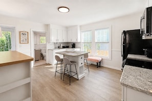 A modern kitchen with white cabinetry, a central island with bar stools, and a black refrigerator. - King Bed Cottage, close to Swamp Rabbit + Downtown (Greenville)
