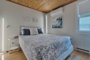 A bedroom with a bed, a bedside table, a wall-mounted air conditioner, and a window.