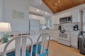 A modern kitchen with white cabinets, a stainless steel oven, and a microwave. There is a dining table with chairs and a decorative wall sign.