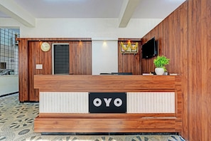 Un mostrador de recepción con detalles de madera, un reloj, un televisor de pantalla plana y una planta en maceta.