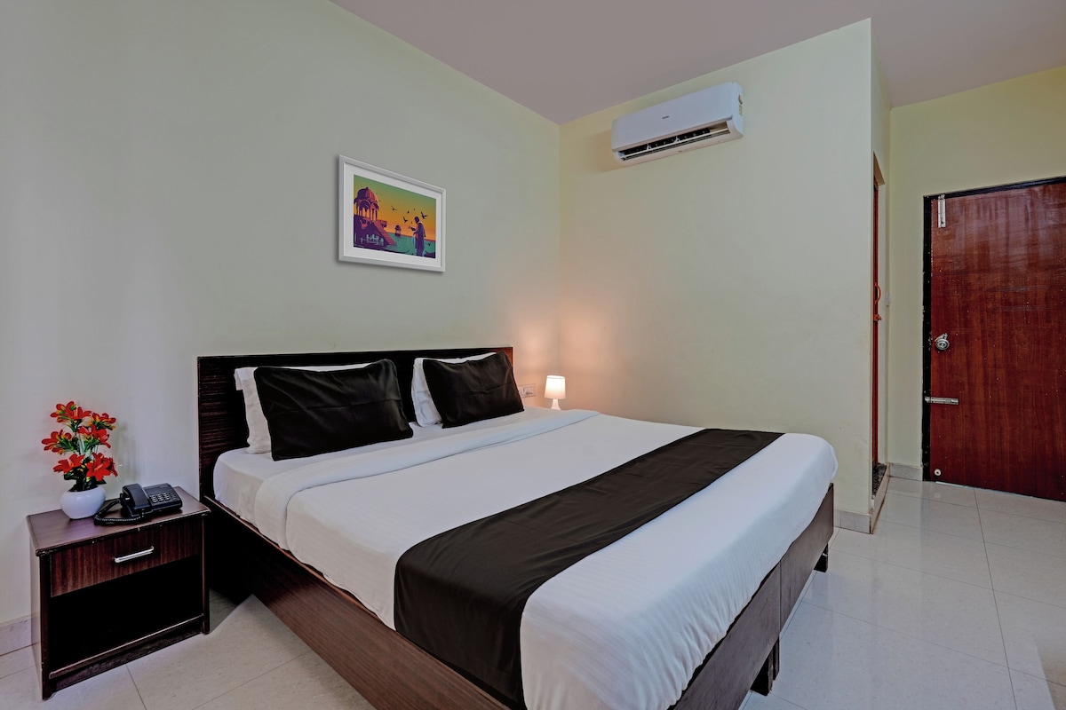 Una habitación de hotel con cama, mesita de noche con teléfono, aire acondicionado de pared y una puerta.