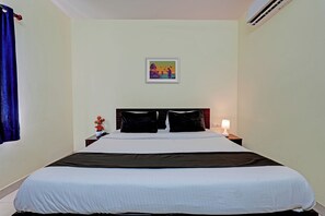 Habitación de hotel con cama, mesita de noche, lámpara, un cuadro en la pared y ventana con cortina.