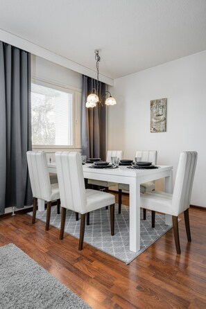 Uma sala de jantar com uma mesa branca posta para quatro pessoas, cercada por cadeiras brancas com pés escuros.