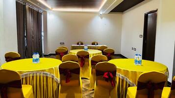 A conference room with round tables, yellow tablecloths, and chairs with red sashes.