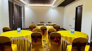 A conference room with round tables, yellow tablecloths, and chairs with red sashes. - Hotel Ambaari Inn (Mandya)
