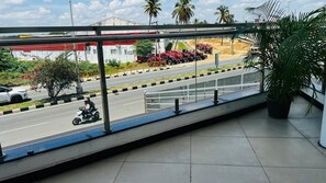 A balcony with a view of a road, a parked motorcycle, and a row of red tractors. - Hotel Ambaari Inn (Mandya)