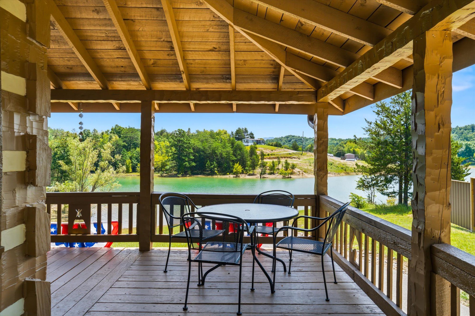 Un espace extérieur abrité, doté d’une table et de chaises, qui offre une vue sur un plan d’eau et sur la verdure.