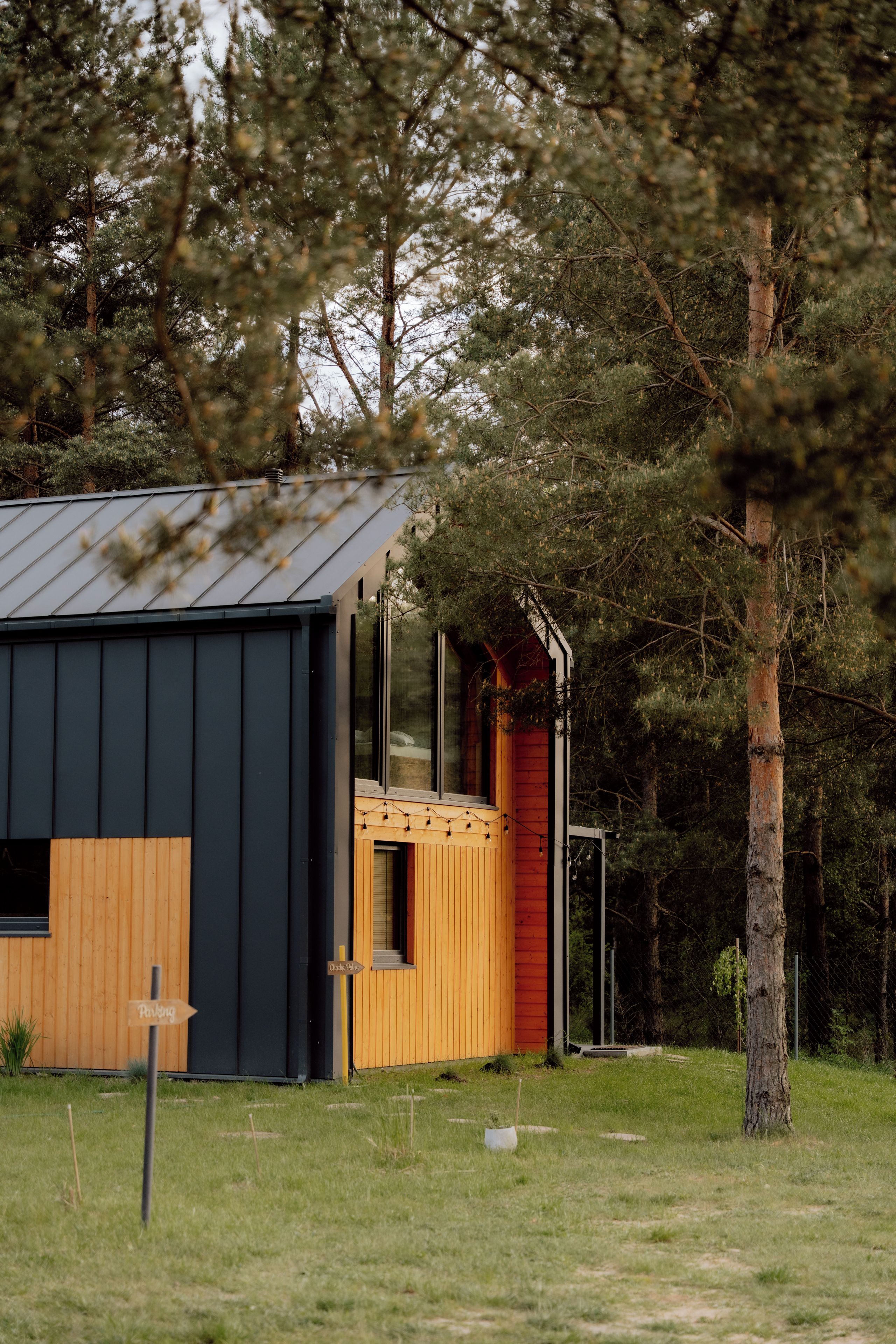 En moderne bygning med mørk facade, træterrasse og rødt dør.