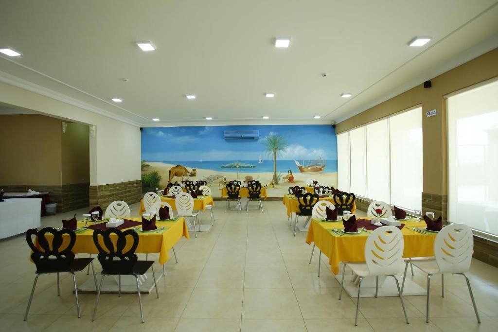 Un área de comedor con mesas y sillas, un mural en la pared y un mostrador de recepción.
