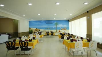 Un área de comedor con mesas y sillas, un mural en la pared y un mostrador de recepción.