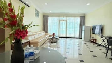 Habitación de hotel con una mesa redonda de vidrio, un sofá, un televisor y un ventanal con cortinas.