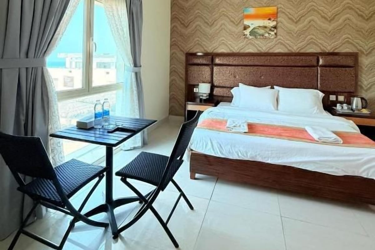 A hotel room with a bed, a table with chairs, a window with curtains, and a wall with a patterned design.
