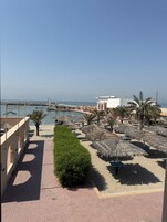 Un paseo marítimo frente a la playa con palmeras, sombrillas de paja y una vista despejada del mar.