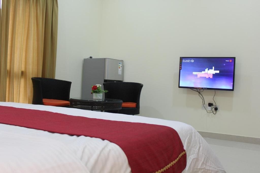 A hotel room with a bed, a television mounted on the wall, a small table with a vase of flowers, and a chair.