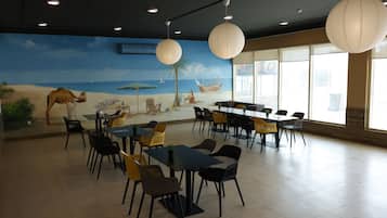 A dining area with tables and chairs, a mural of a beach scene, and large paper lanterns.
