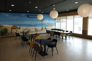 Un comedor con mesas y sillas, un mural con una escena de playa y grandes farolillos de papel.