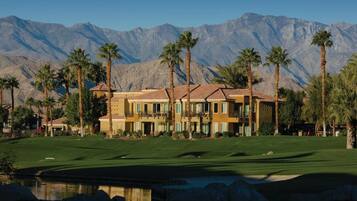 A multi-story building with balconies, a golf course, and palm trees.