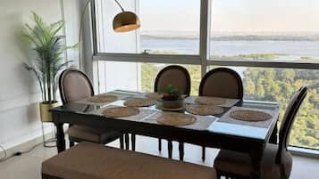 A dining area with a table set for four, large windows, and a view of a body of water.