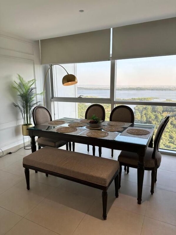 Un comedor con una mesa dispuesta para cuatro personas, ventanas amplias y vista a un cuerpo de agua.