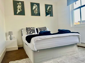 A bedroom with a bed, pillows, a nightstand, a lamp, and artwork on the wall. - Charming London Apartment With 2 Bedrooms (London)
