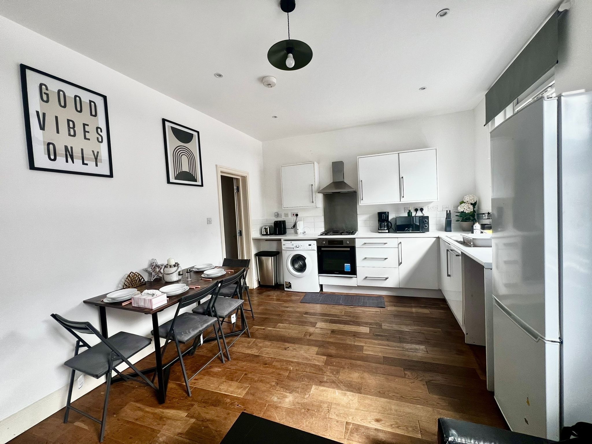 Une cuisine compacte avec un coin repas, des meubles blancs et un tableau encadré de noir accroché au mur.