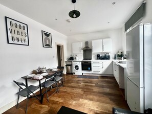 A compact kitchen with a dining area, white cabinetry, and a black-framed picture on the wall. - Charming London Apartment With 2 Bedrooms (London)