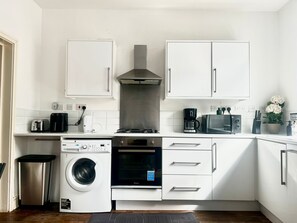 Een compacte keuken met een wasmachine, oven, magnetron en koffiezetapparaat.