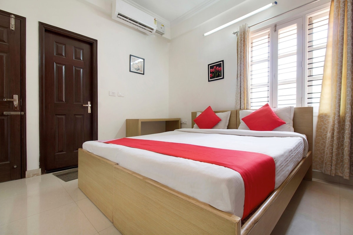 Quarto de hotel com cama, guarda-roupa, mesa de cabeceira, aparelho de ar condicionado e janela com cortinas.