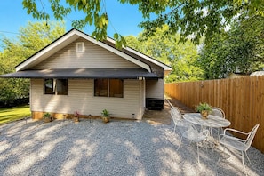 A single-story house with a gravel driveway, a wooden fence, and a patio with outdoor furniture. - Cozy Greenville Cottage | 2 Queens + Near Downtown (Greenville)